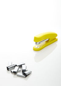 Close-up of yellow stapler with pins on white background