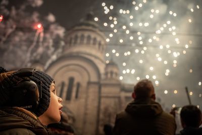 Child wearing noice cancelation headphones while fireworks in the sky