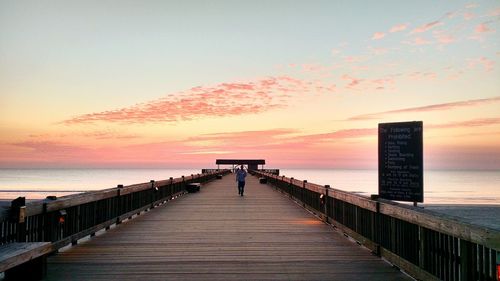 Man walking on pier over sea against sky during sunset