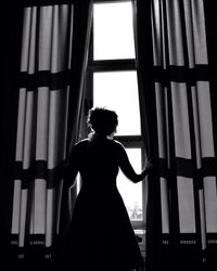 Silhouette of woman looking through window