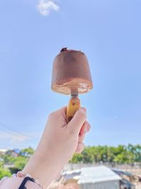 Midsection of person holding ice cream against sky