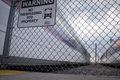 Close-up of text on chainlink fence against sky