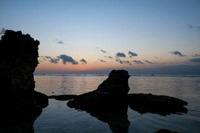 Silhouette rocks on sea against sky during sunset