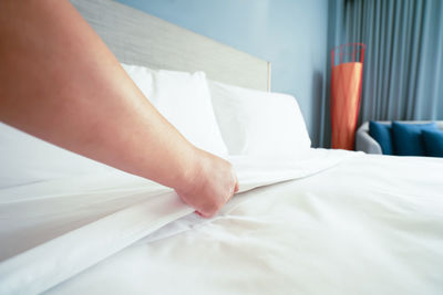 Cropped hand of woman arranging sheet on bed at home