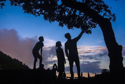 Silhouette people standing by tree against sky during sunset
