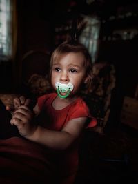 Innocent girl with pacifier in mouth looking away at home