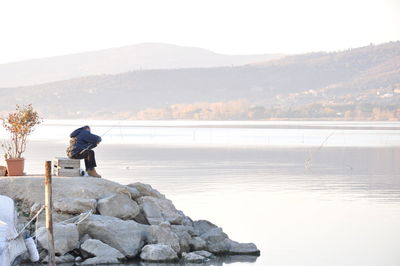 Woman fishing in lake against sky