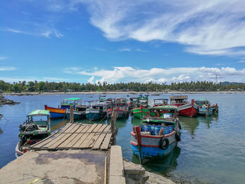 Fishing boats moored at harbor against sky