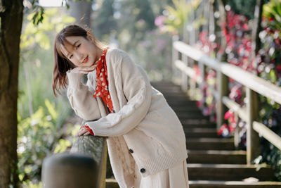 Portrait of young woman standing against fence