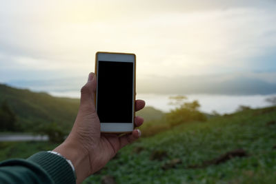 Close-up of hand holding smart phone against sky
