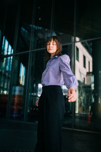 Low angle portrait of beautiful young woman standing against glass wall