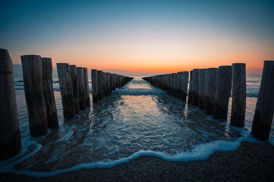 Wooden posts in sea against sky during sunset