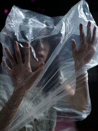 Portrait of young woman wearing plastic against black background