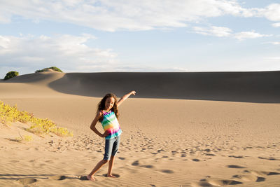 Full length of girl posing on sand at beach against sky
