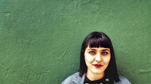 Portrait of a beautiful young woman standing against green wall