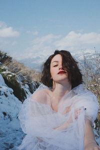 Portrait of young woman standing on mountain against sky during winter