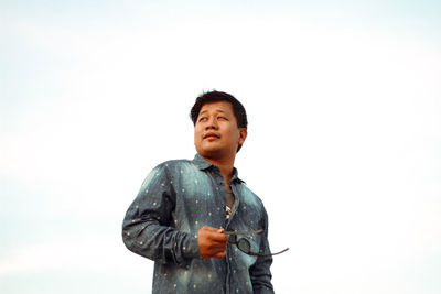 Low angle view of young man standing against sky