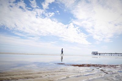 Person walking on beach against cloudy sky