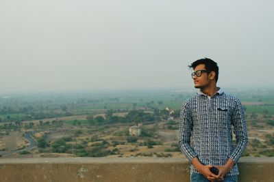 Man looking away while leaning on retaining wall against sky