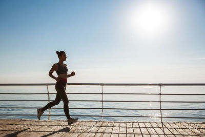 Full length of woman running by railing against sea