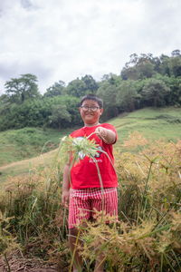 Portrait of boy standing amidst plants against sky