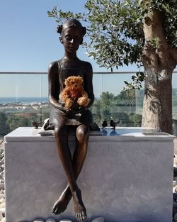 Man sitting by statue against sky