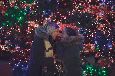 Female friends eating caramelized apple during christmas at night