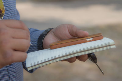 Midsection of man with smart phone writing in diary while standing outdoors