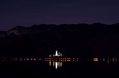 Silhouette illuminated buildings by sea against sky at night