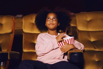 Girl holding food while sitting on chair in movie theater