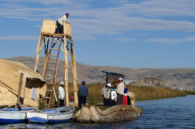 People sitting on deck chair by lake against sky