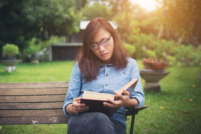 Young woman reading book while sitting on park bench