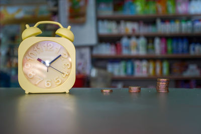 Close-up of yellow clock and coins on table 