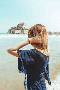 Rear view of woman standing at beach against sky