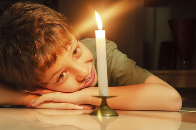 Child looking at a lit candle lying on the floor of the house. 