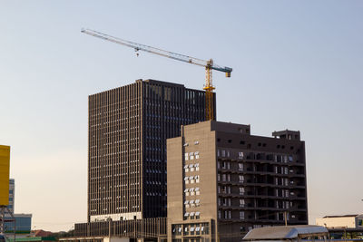 Low angle view of crane and buildings against clear sky