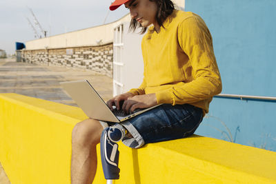 Young man working on laptop while sitting on wall