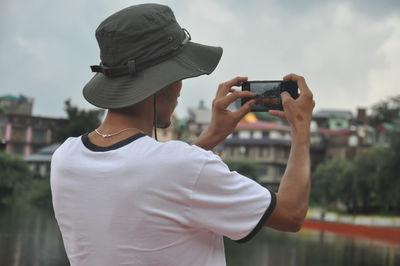 Back view of a male tourist taking photo of landscape with smartphone during cloudy weather 