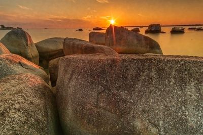 Close-up of rocks in sea against sunset sky
