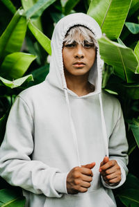 Portrait of smiling young man wearing hood while standing against plants