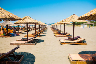 Lounge chairs on beach against clear blue sky