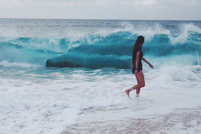 Sea waves rushing towards woman walking on shore