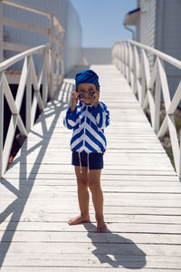 Boy child in a striped blue sailor jacket walks on the street among white wooden houses by the sea