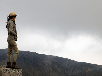 Woman standing on rock while looking at rocky mountain against sky