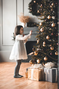 Full length of girl standing by christmas tree at home