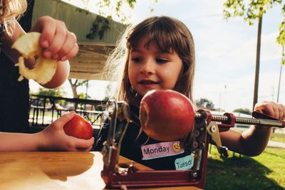 Cute girl holding fruit peeler on table outdoors