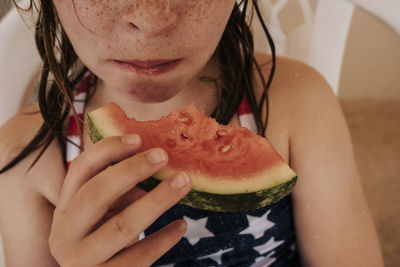 Midsection of wet girl eating watermelon while sitting on chair