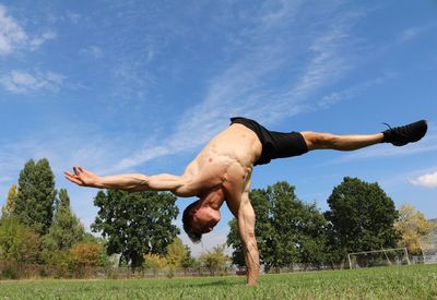 Shirtless man doing handstand on field against sky