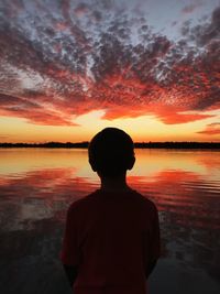 Rear view of silhouette man standing in front of lake