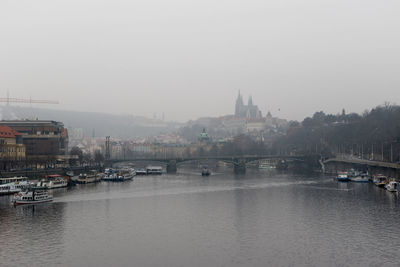 Boats in river by buildings in city against sky